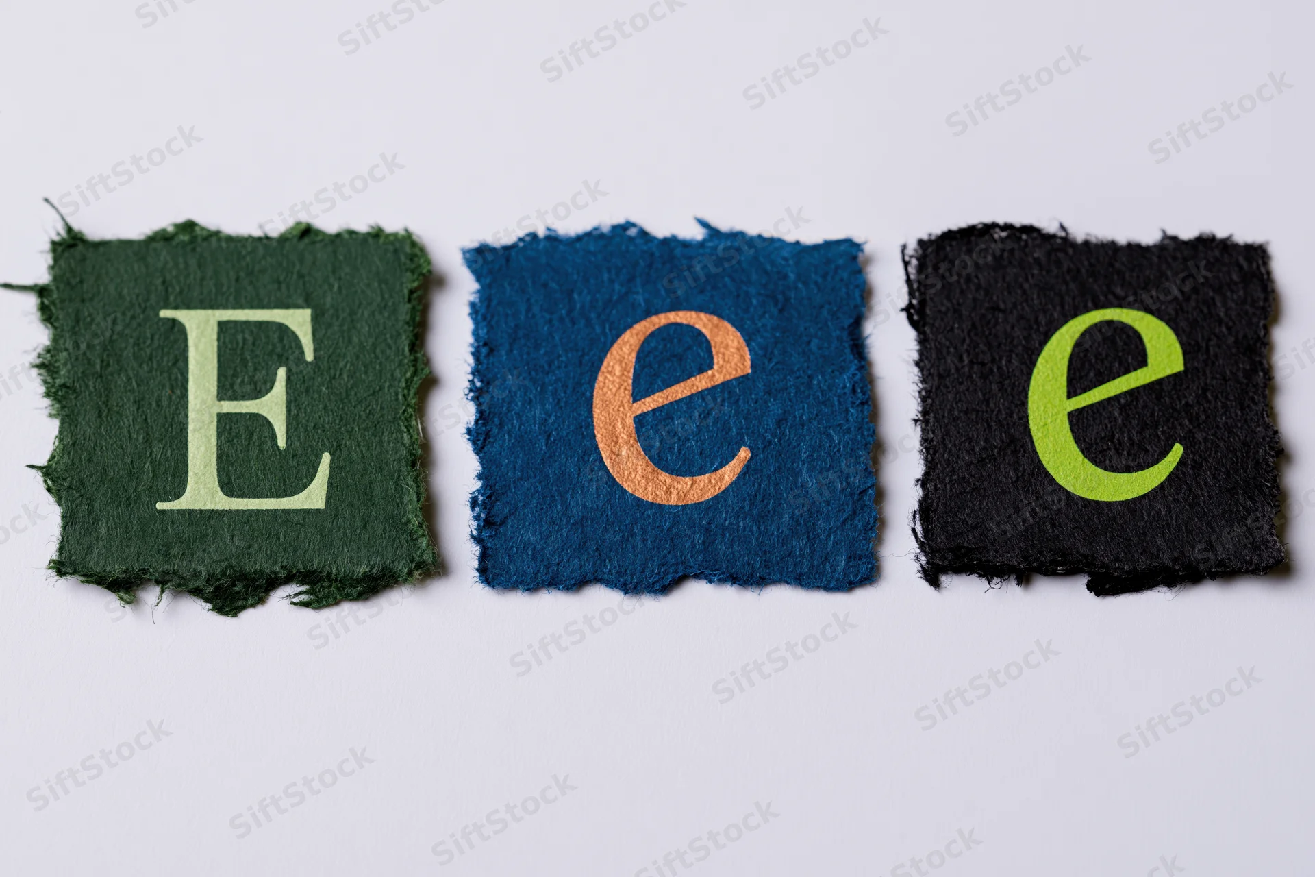 Three torn paper scraps with letters e in different colors and cases arranged in a row on white background