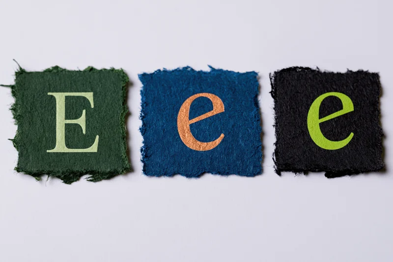 Three torn paper scraps with letters e in different colors and cases arranged in a row on white background