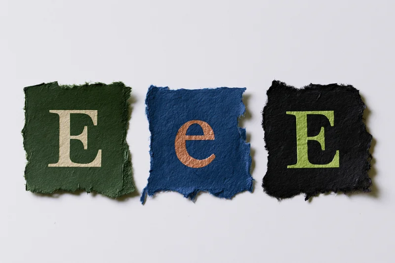 Three torn paper scraps with the letter e in different colors and cases arranged in a row on a white background