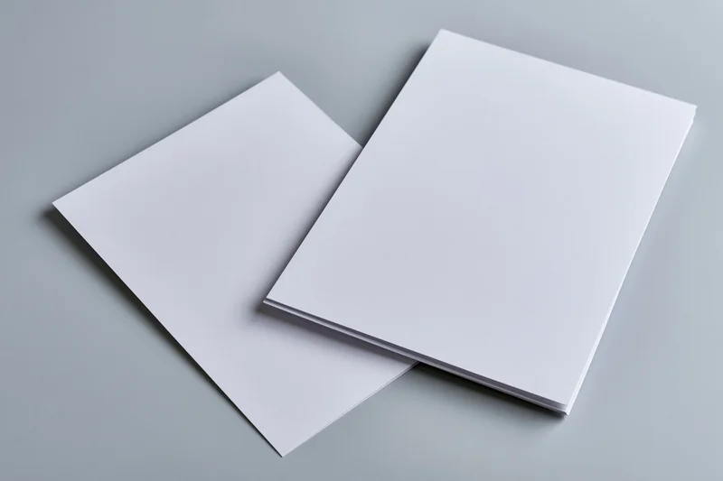 Two blank white a4 paper sheets stacked offset on a gray surface