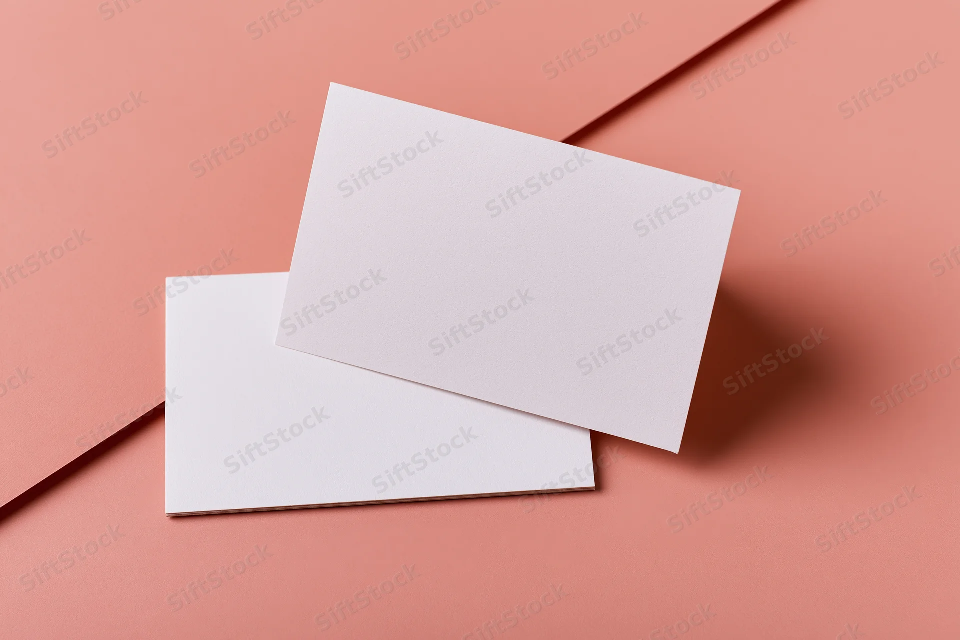 Two blank white rectangular cards arranged on a pink surface in a flat lay composition
