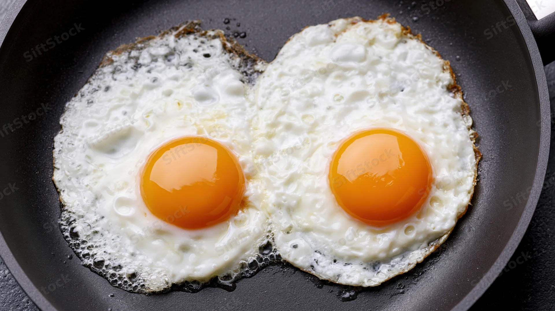 Two sunny-side-up eggs frying in a nonstick skillet