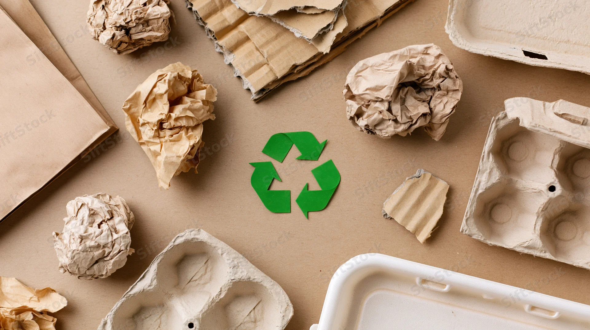 Recyclable paper and cardboard waste arranged flat on brown surface with green recycling symbol