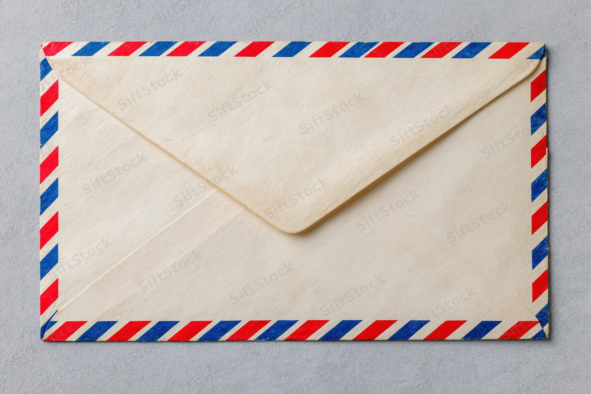Vintage airmail envelope with red and blue diagonal stripes lying flat on gray surface