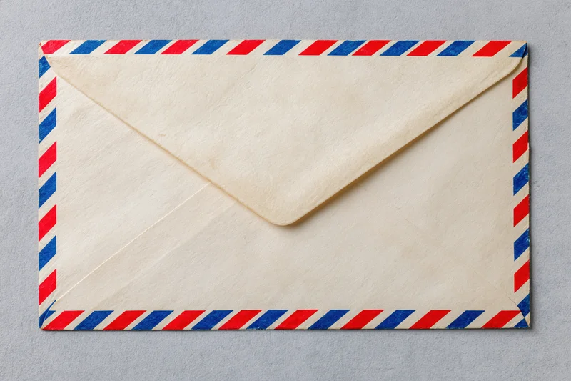 Vintage airmail envelope with red and blue diagonal stripes lying flat on gray surface