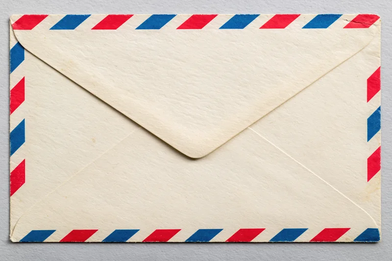 Vintage airmail envelope with red and blue diagonal stripes lying flat on a neutral surface