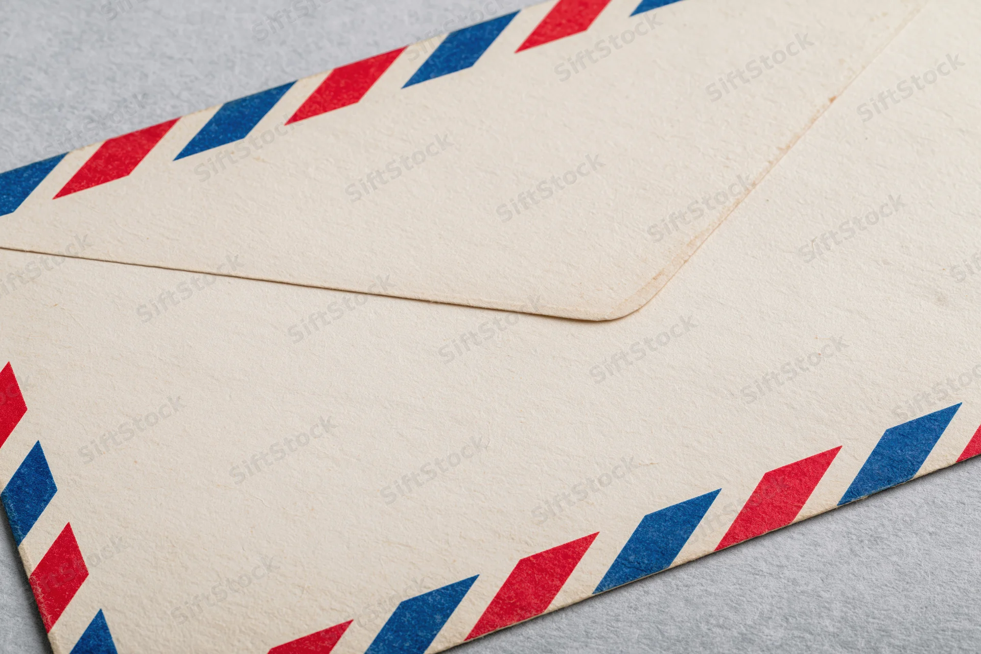 Vintage airmail envelope with red and blue diagonal stripes lying flat on gray surface