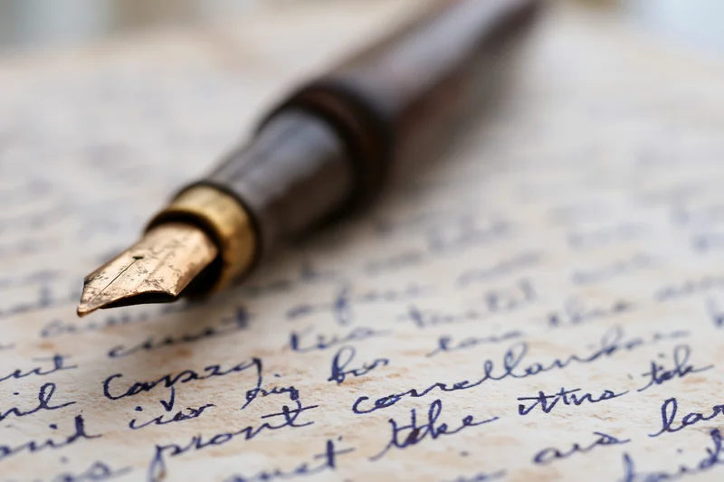 Vintage brass-nibbed fountain pen resting on handwritten letter with cursive script