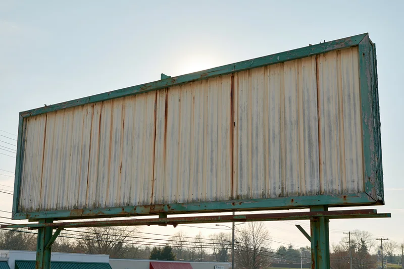 Weathered roadside billboard with blank letterboard under clear sky