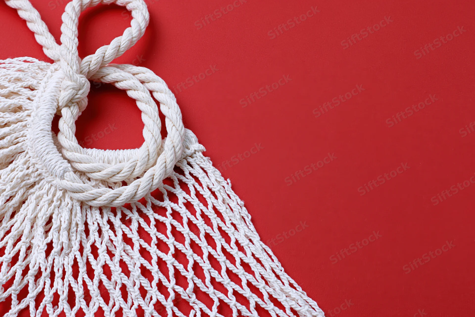 White cotton mesh string bag with knots and fringe on red background