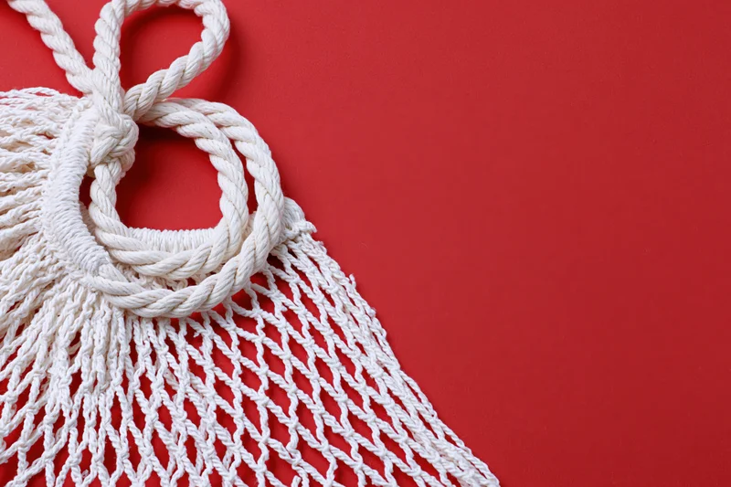 White cotton mesh string bag with knots and fringe on red background