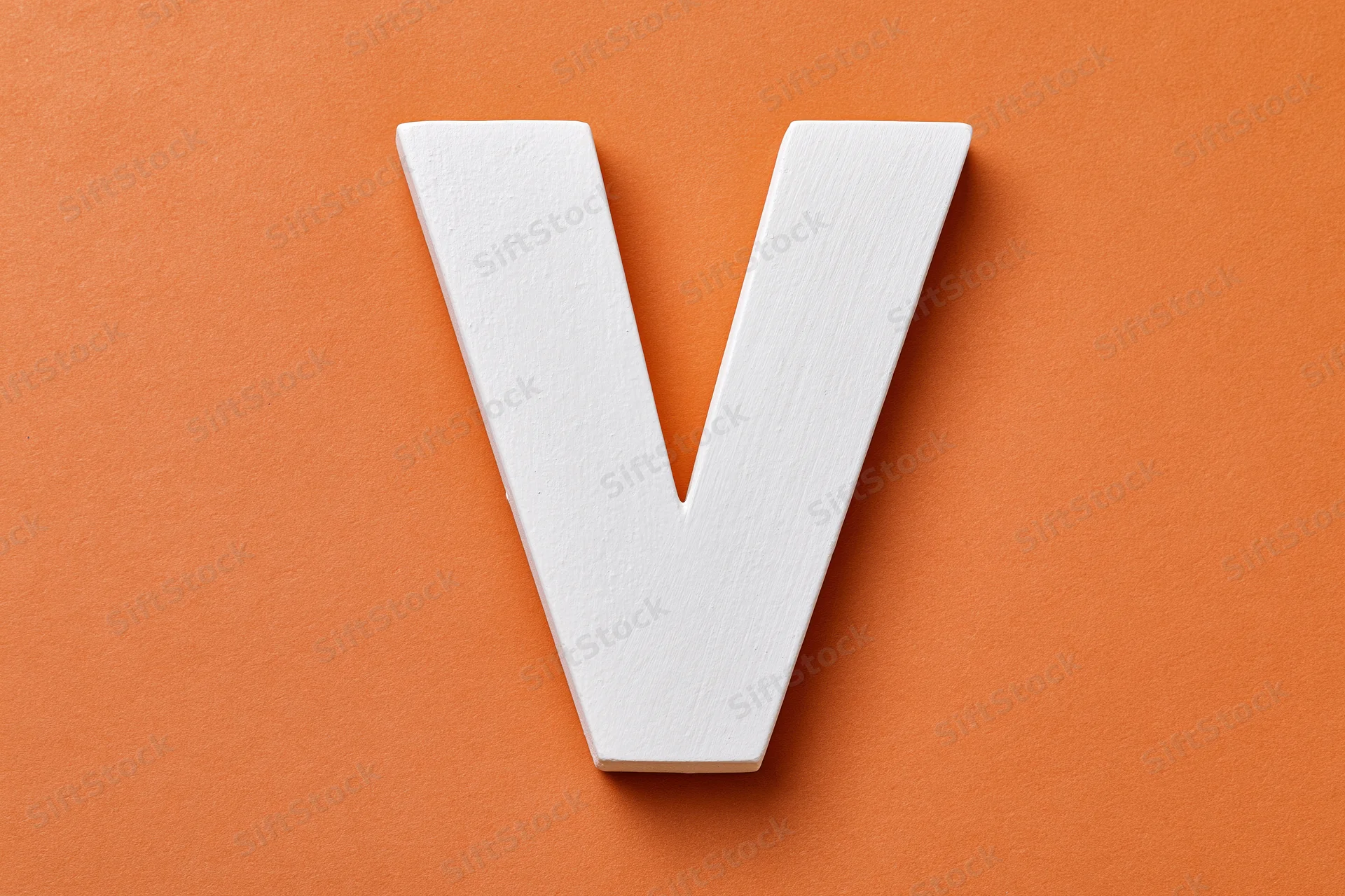 White painted wooden letter v centered on orange textured surface