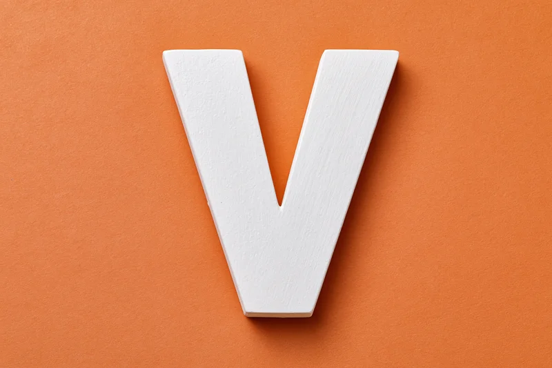 White painted wooden letter v centered on orange textured surface