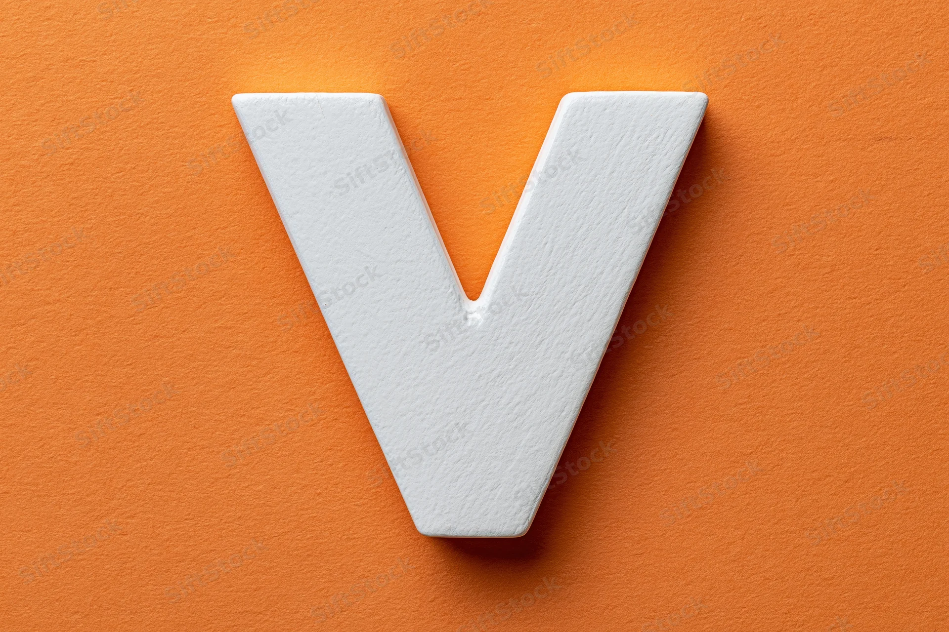 White painted wooden letter v centered on orange textured surface