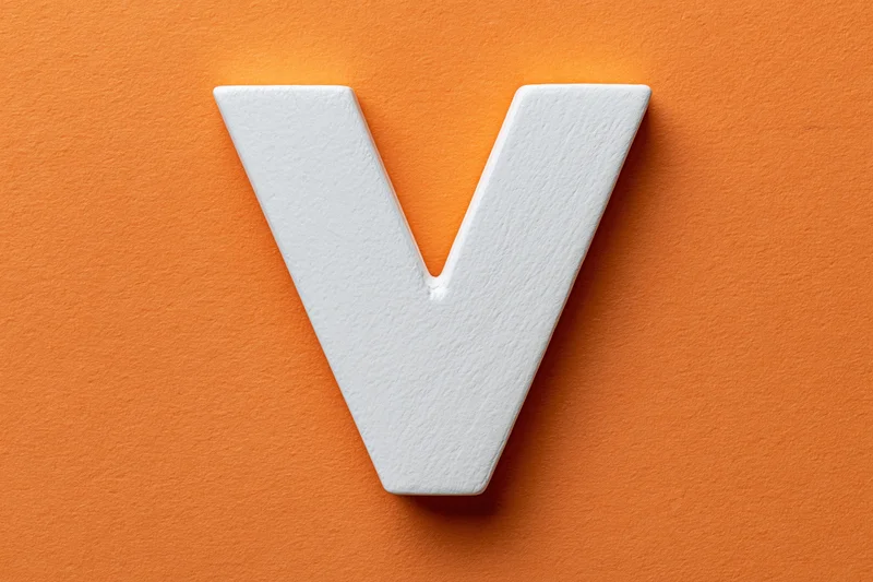 White painted wooden letter v centered on orange textured surface
