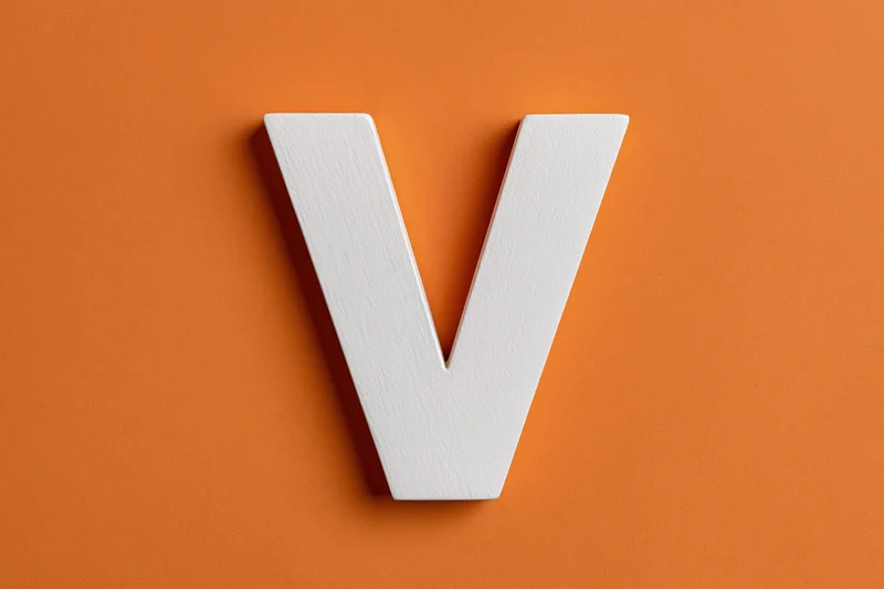 White painted wooden letter v centered on orange textured surface