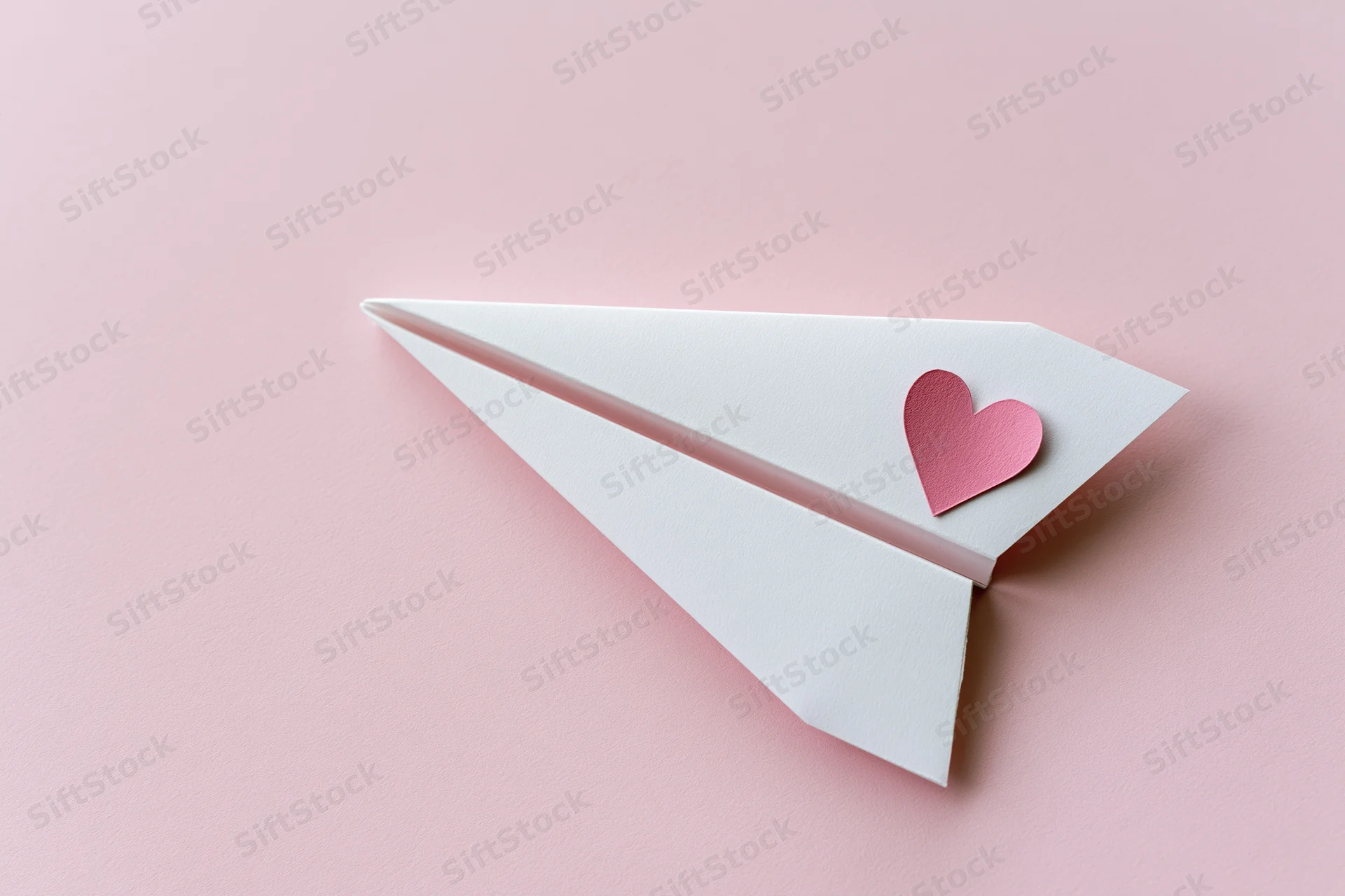 White paper airplane with pink heart sticker on pink surface