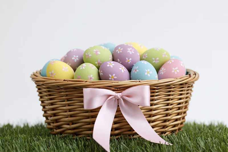 Wicker basket filled with pastel painted easter eggs decorated with floral patterns on green grass