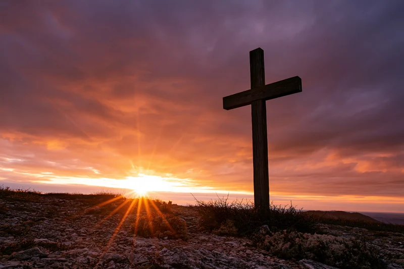 Wooden christian cross silhouetted on rocky hilltop at sunset