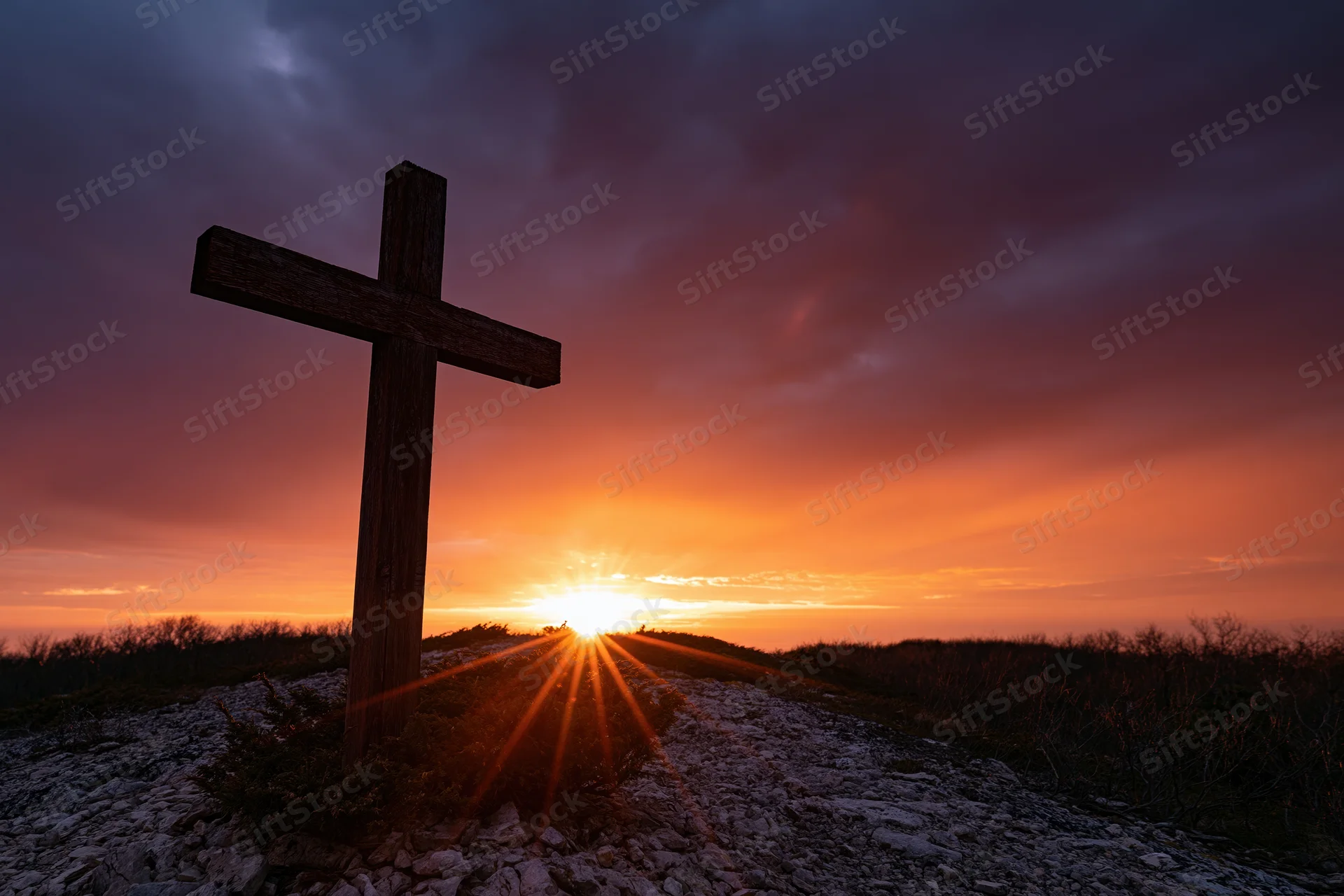 Wooden christian cross silhouetted on rocky hilltop at sunset