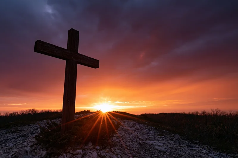 Wooden christian cross silhouetted on rocky hilltop at sunset