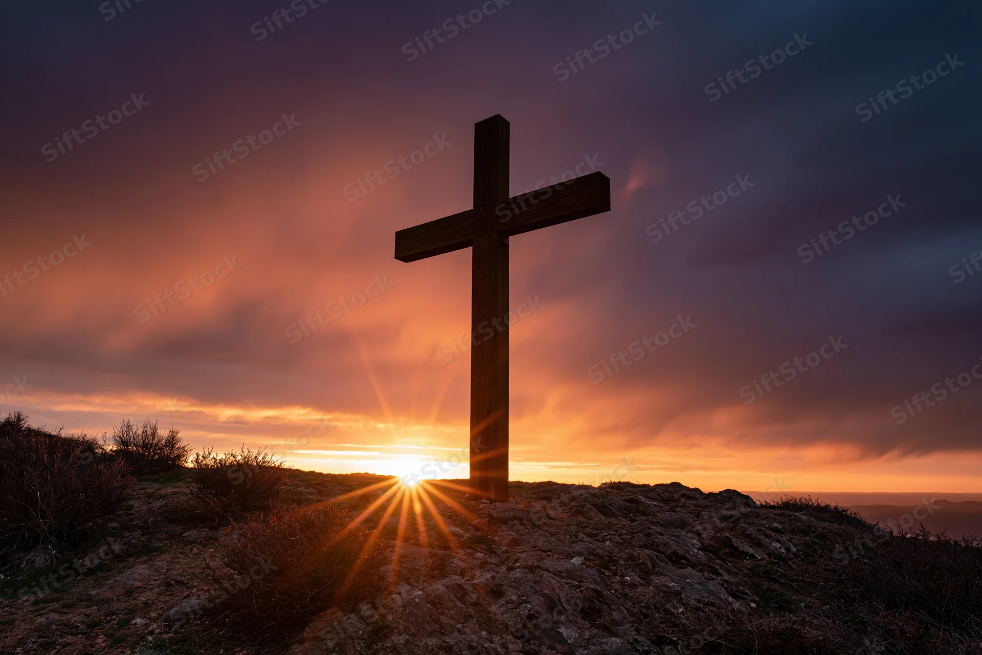 Wooden christian cross silhouetted on rocky hilltop at sunset