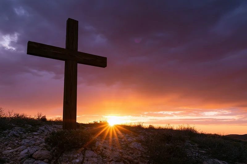 Wooden christian cross silhouetted on rocky hilltop at sunset
