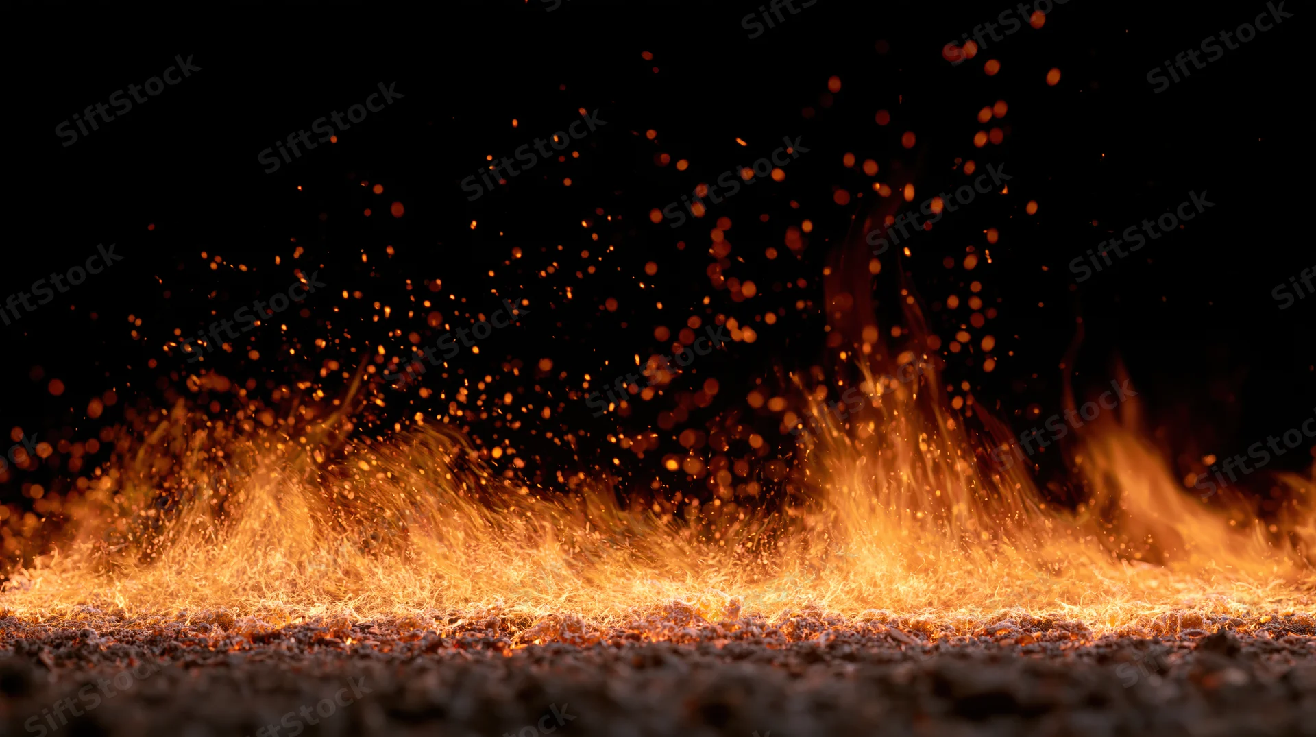 Horizontal line of intense flames burning across a dark ground with flying sparks