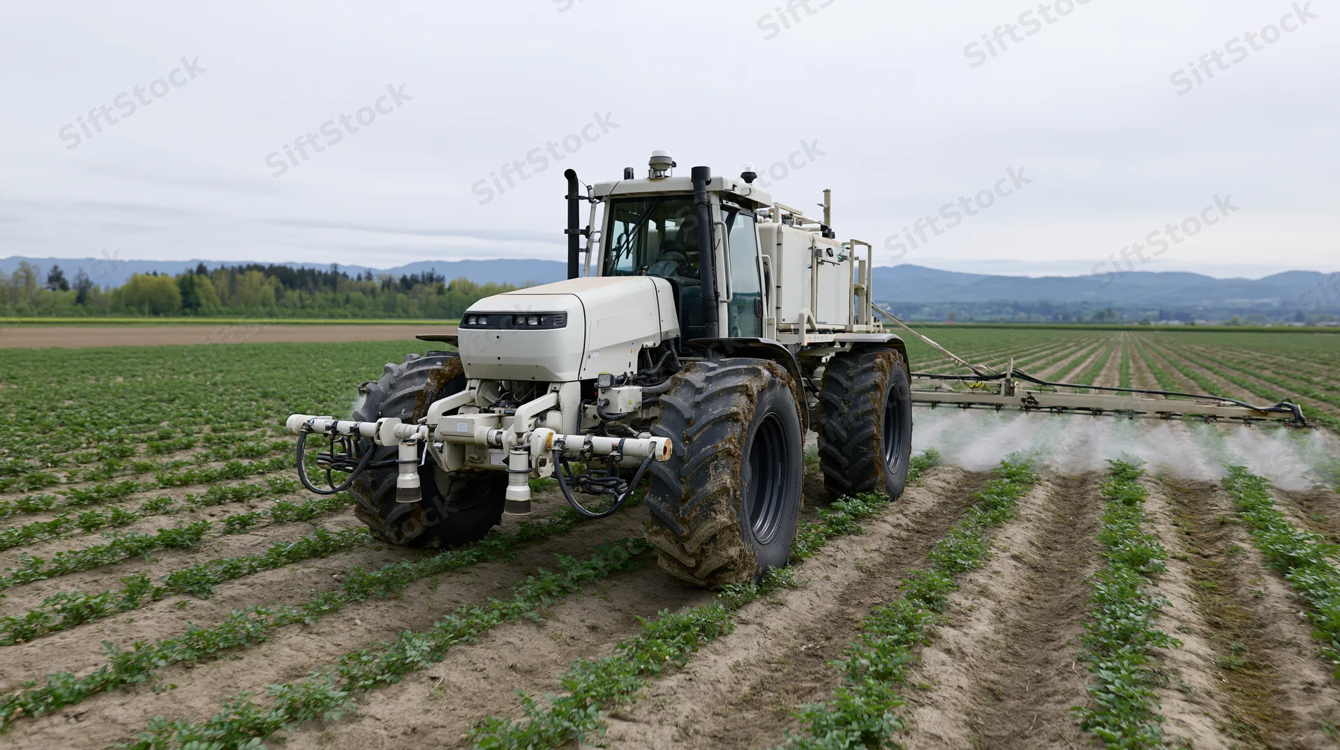 Autonomous tractor spraying crops in a field with rows of green plants under overcast sky