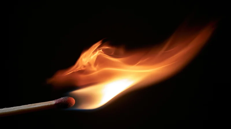Lit match burning with bright orange flame against black background
