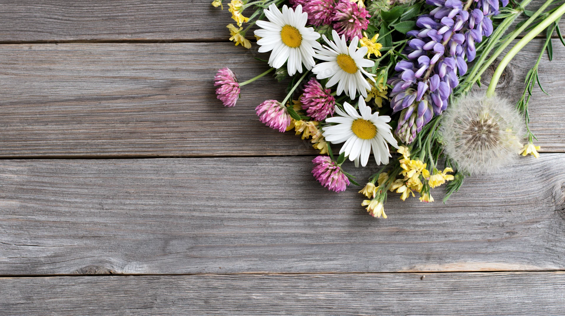 Wildflowers arranged in a loose cluster on a weathered wooden table with copyspace
