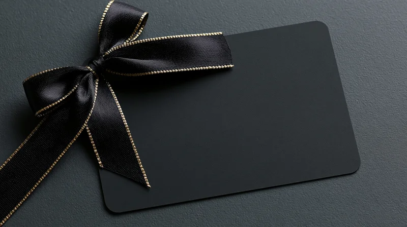 Matte black gift card with black ribbon bow lying flat on dark textured surface
