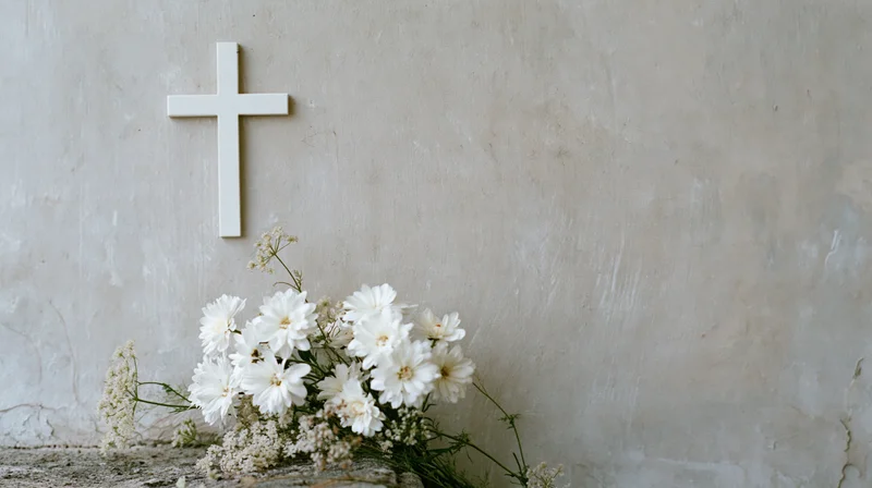 White christian cross on textured wall with white flowers arranged below
