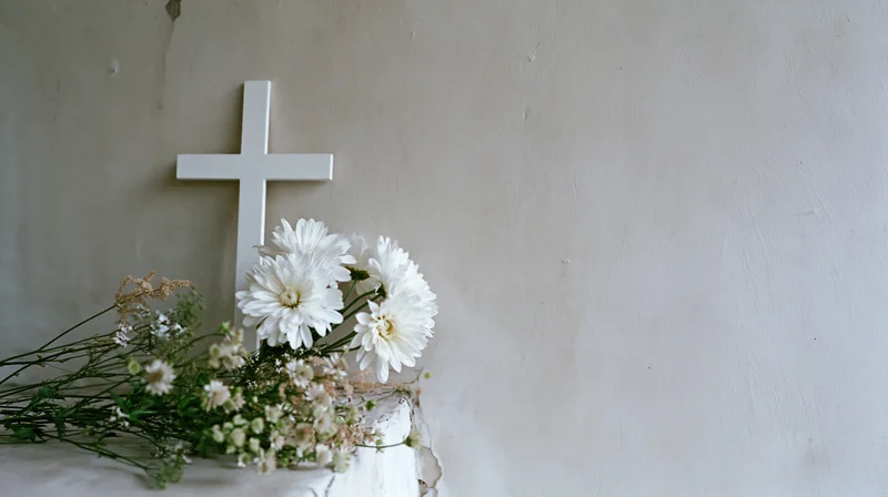 White christian cross with white flowers and greenery on a textured wall