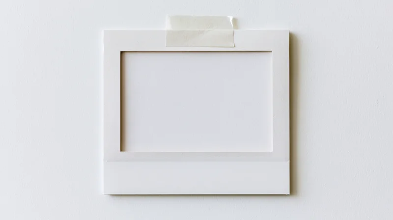 Blank white polaroid frame taped to a wall with adhesive tape, centered on a plain surface