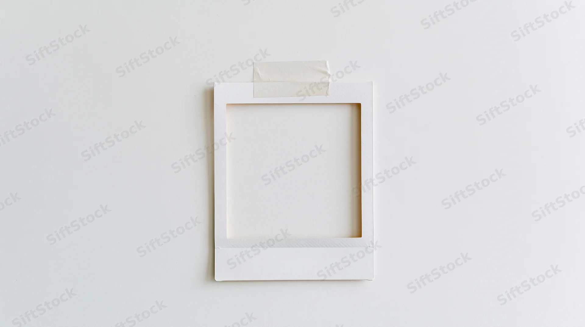 Blank white polaroid frame taped to a plain wall with copyspace
