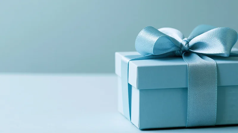 Light blue gift box with satin ribbon bow on plain surface