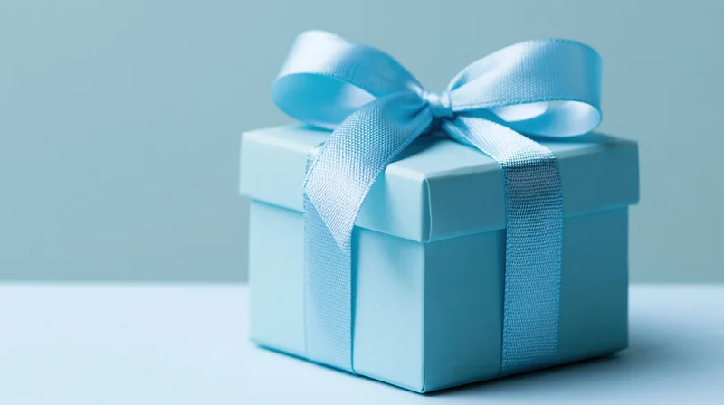 Light blue gift box with satin ribbon bow on plain surface