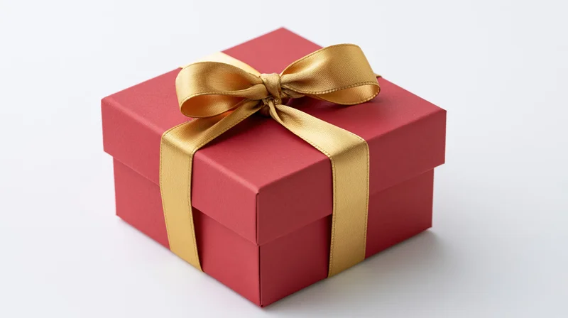 Red gift box wrapped with gold satin ribbon and bow on white background