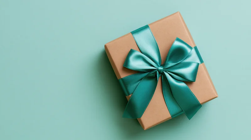 Square gift box wrapped in brown kraft paper with teal satin ribbon bow on teal background