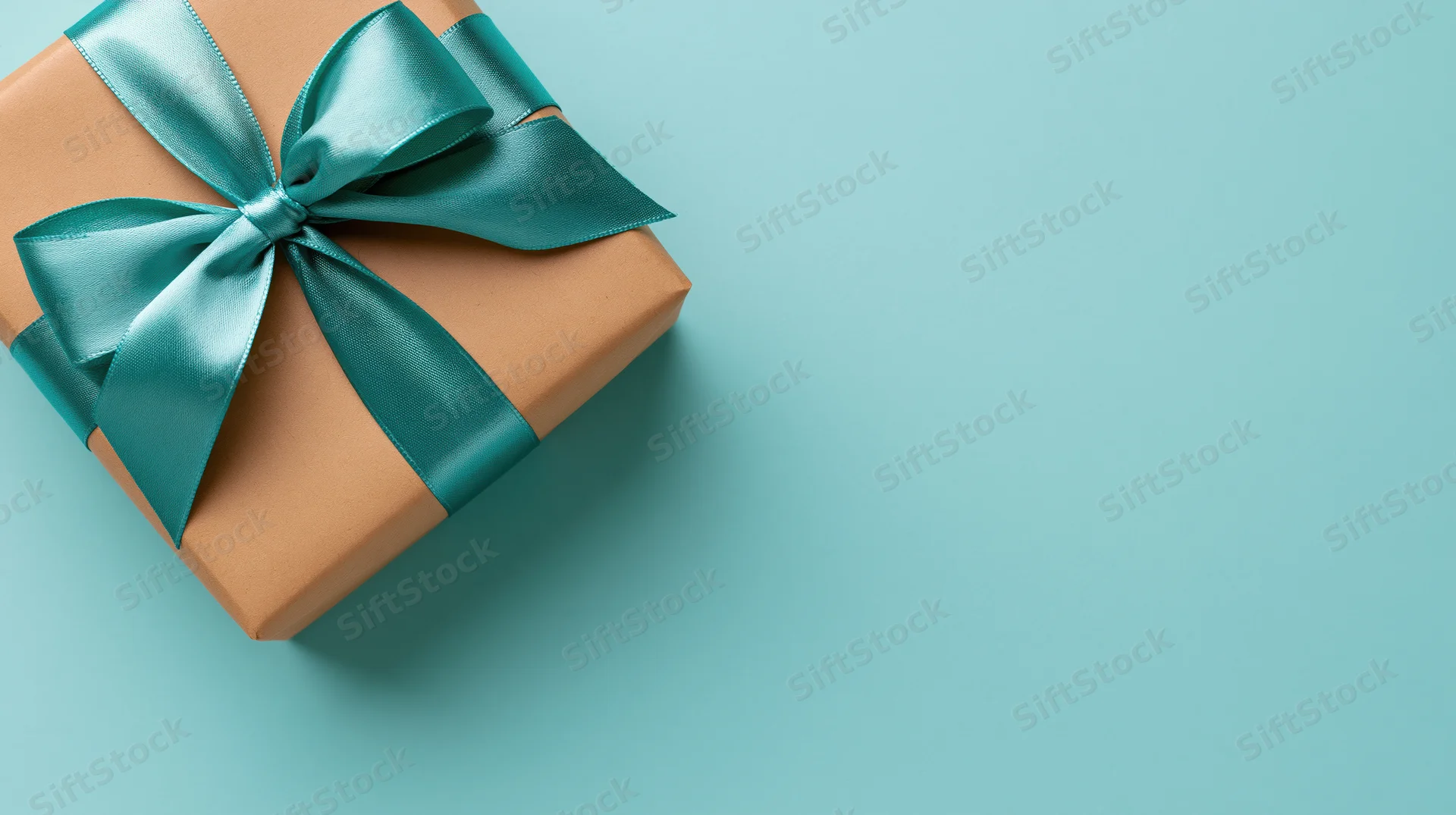 Square gift box wrapped in brown kraft paper with teal satin ribbon bow on blue background