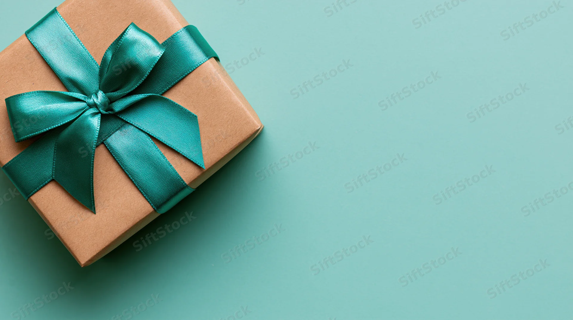 Square gift box wrapped in brown kraft paper with teal ribbon bow on teal surface