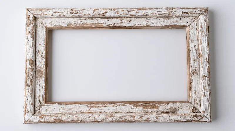 Weathered wooden picture frame with peeling white paint hanging on a white wall