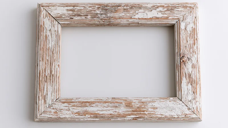 Weathered wooden picture frame with peeling white paint hanging on a white wall