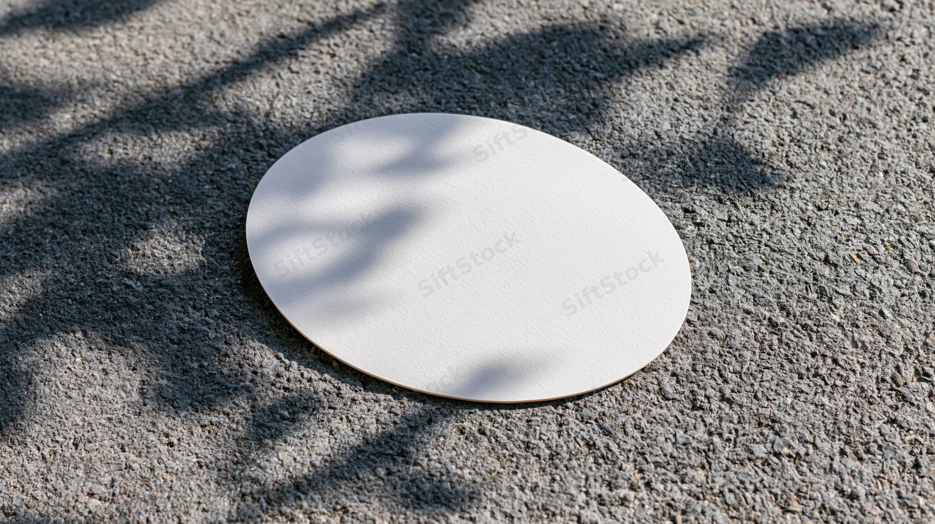 White oval sticker lying flat on rough gray asphalt with tree shadows
