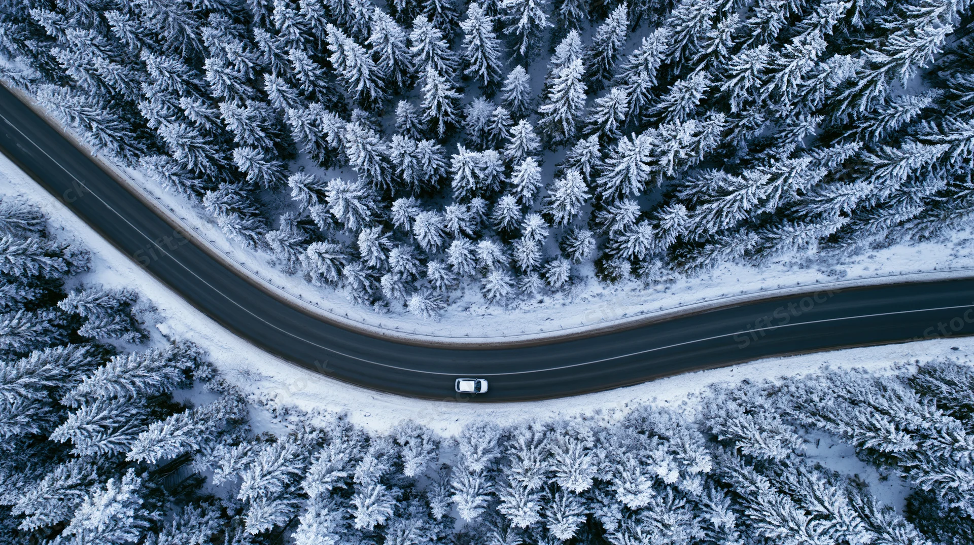 Aerial top-down view of a winding road through a snow-covered forest with a car driving on it