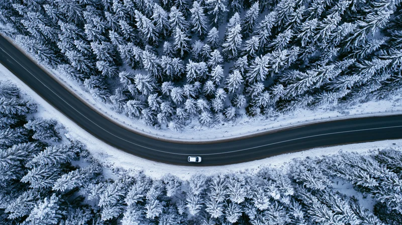 Aerial top-down view of a winding road through a snow-covered forest with a car driving on it