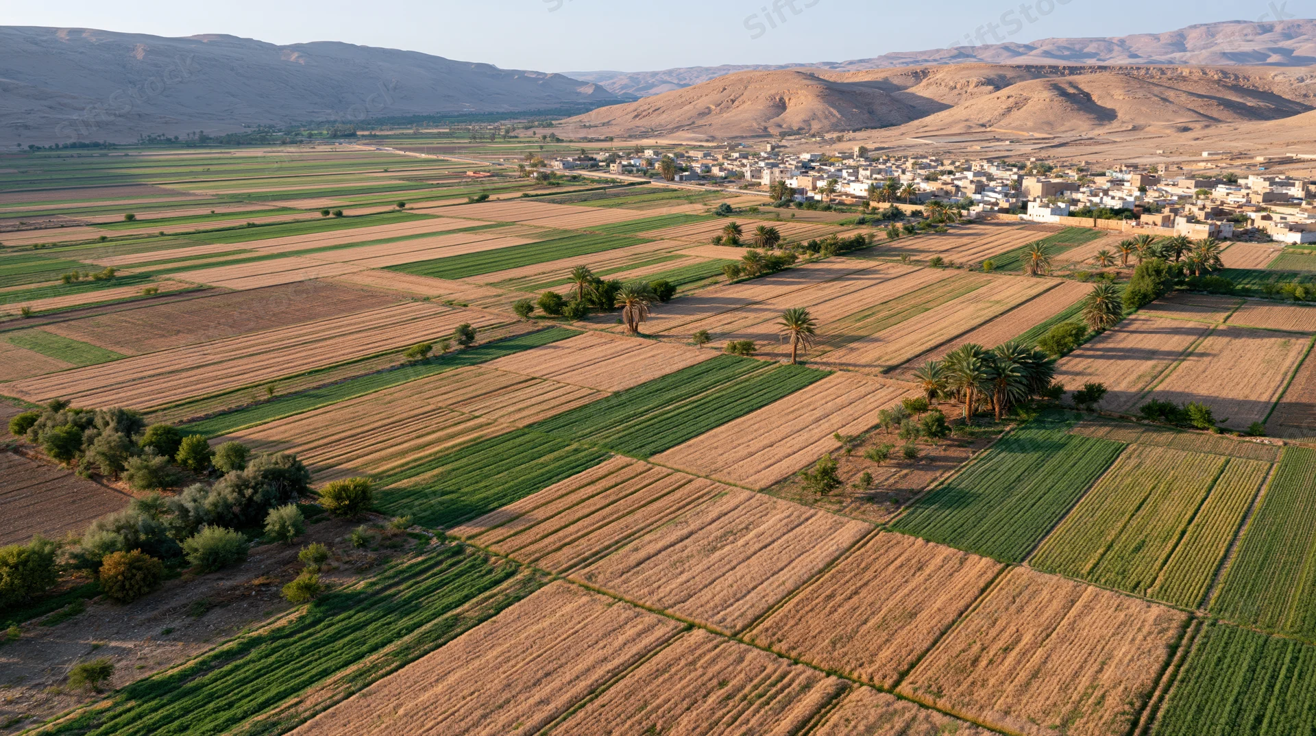 Aerial view of patchwork agricultural fields with a village nestled among mountains in a dry valley