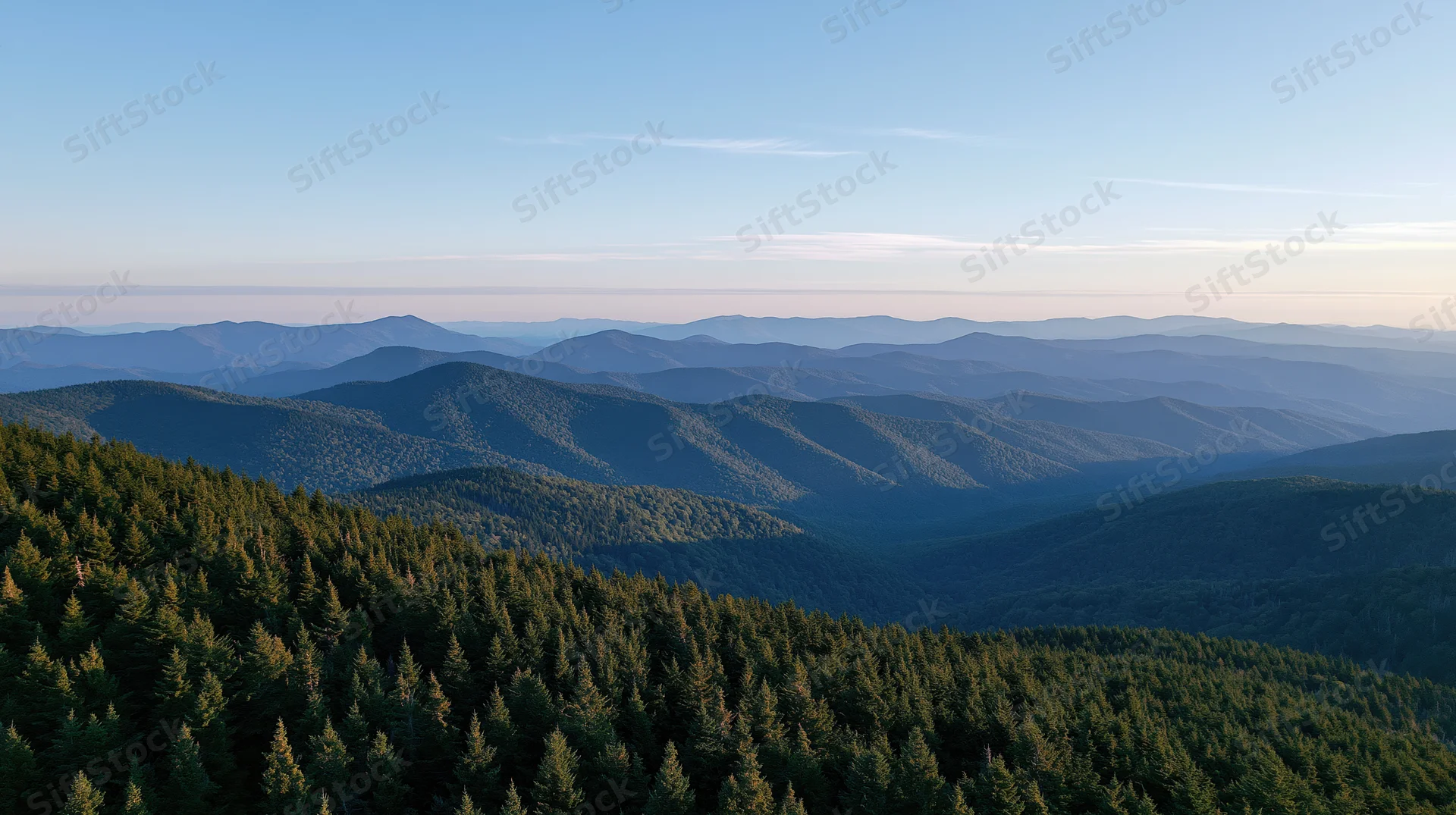 Aerial view of layered forested mountains stretching into the distance under a clear sky