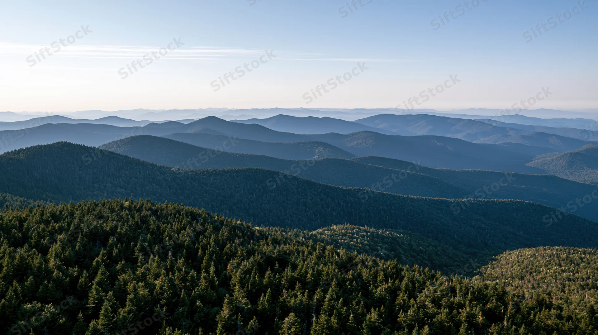 Aerial view of layered forested mountains stretching into the distance under a clear sky